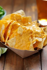 Une portion généreuse de nachos au fromage servis sur une table en bois, accompagnés de tranches de citron vert.