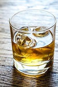 Un verre de whisky doré avec des glaçons, posé sur une table en bois rustique.